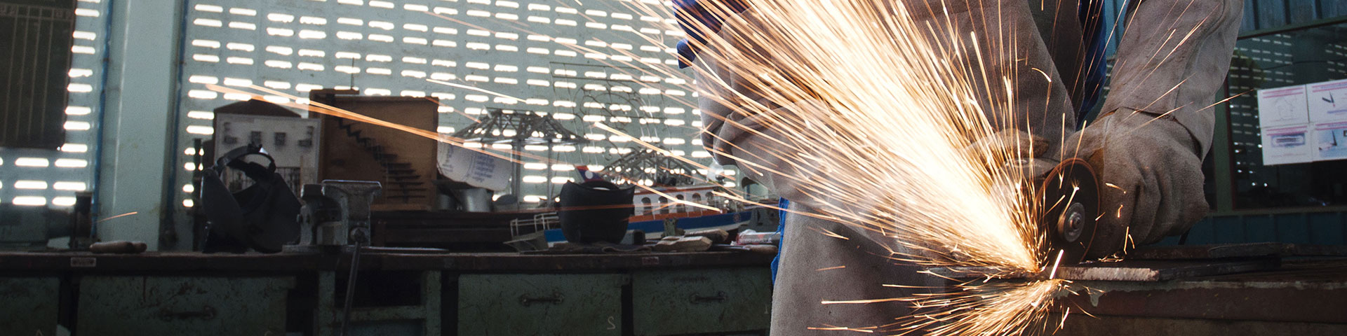 Ein Mensch mit Handschuhen bearbeitet Metall in einer Werkstatt.