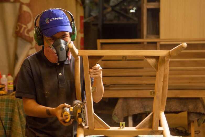 Eine Person, die eine Maske trägt und an einem Stück Holz arbeitet.
