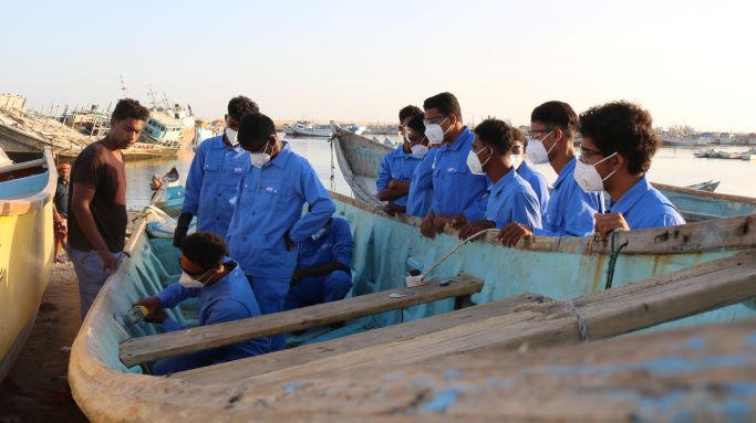 Junge Männer in blauen Uniformen werden geschult, ein Boot zu reparieren.