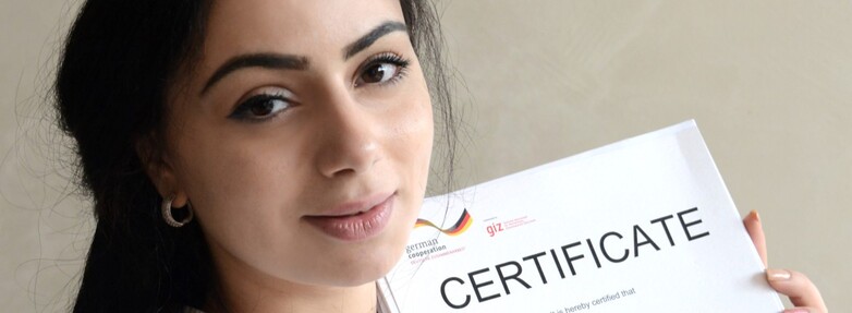 A young woman holds a certificate and smiles.