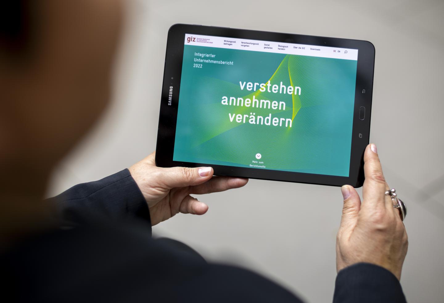 Two hands are holding a tablet computer, which is displaying the intro page of the Integrated Company Report 2022 of GIZ.