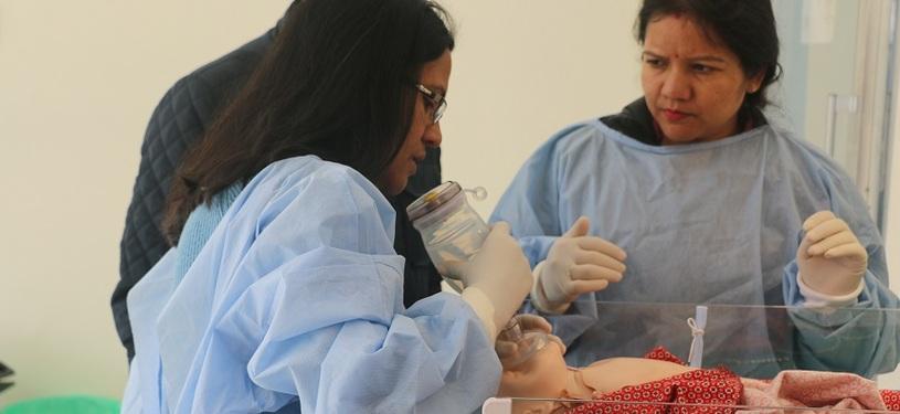Two women and a man stand beside a breathing simulator.