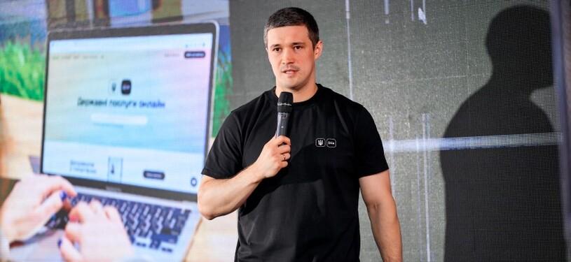A man speaks into a microphone. Behind him is a presentation on digitalisation.