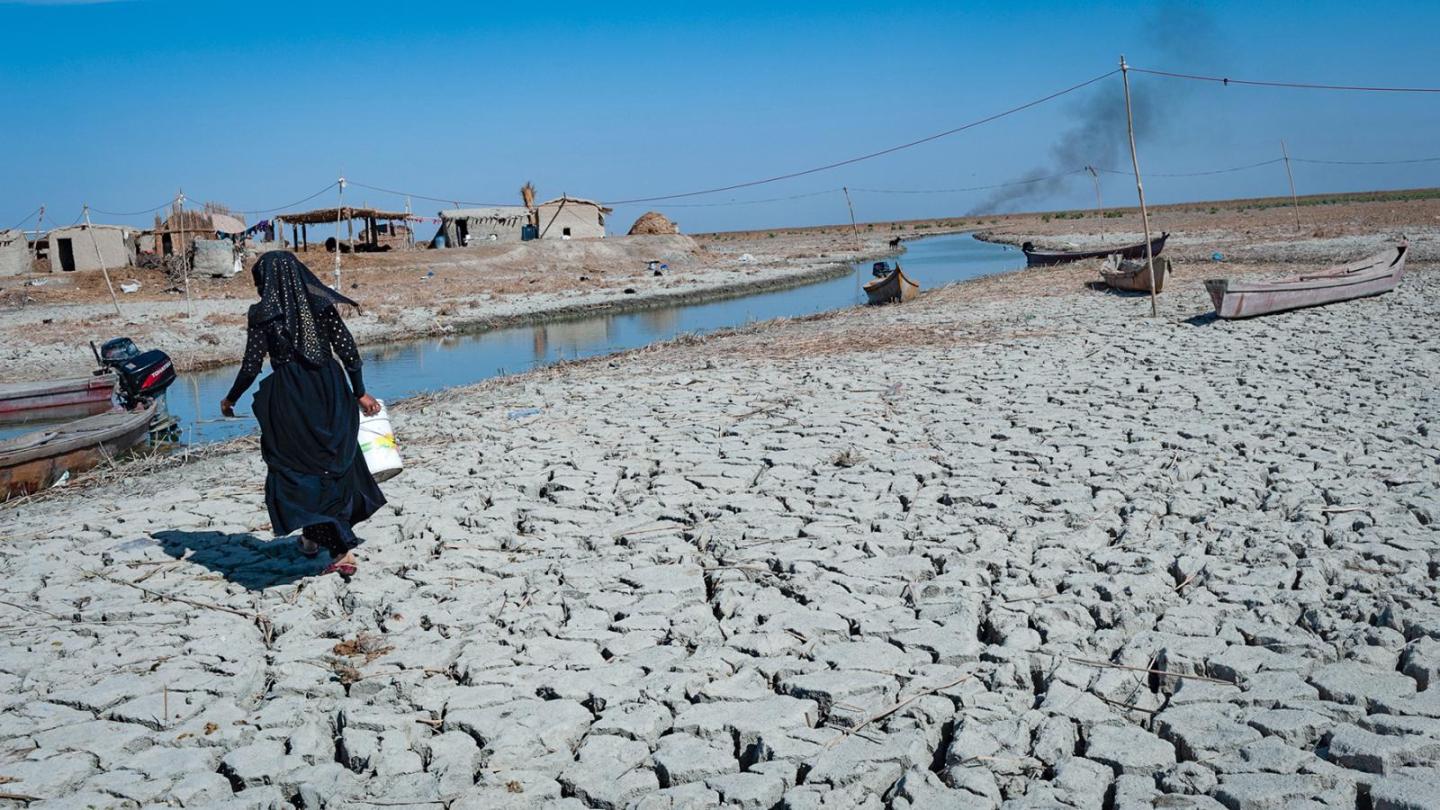 A woman in a robe walks across a rocky desert landscape.