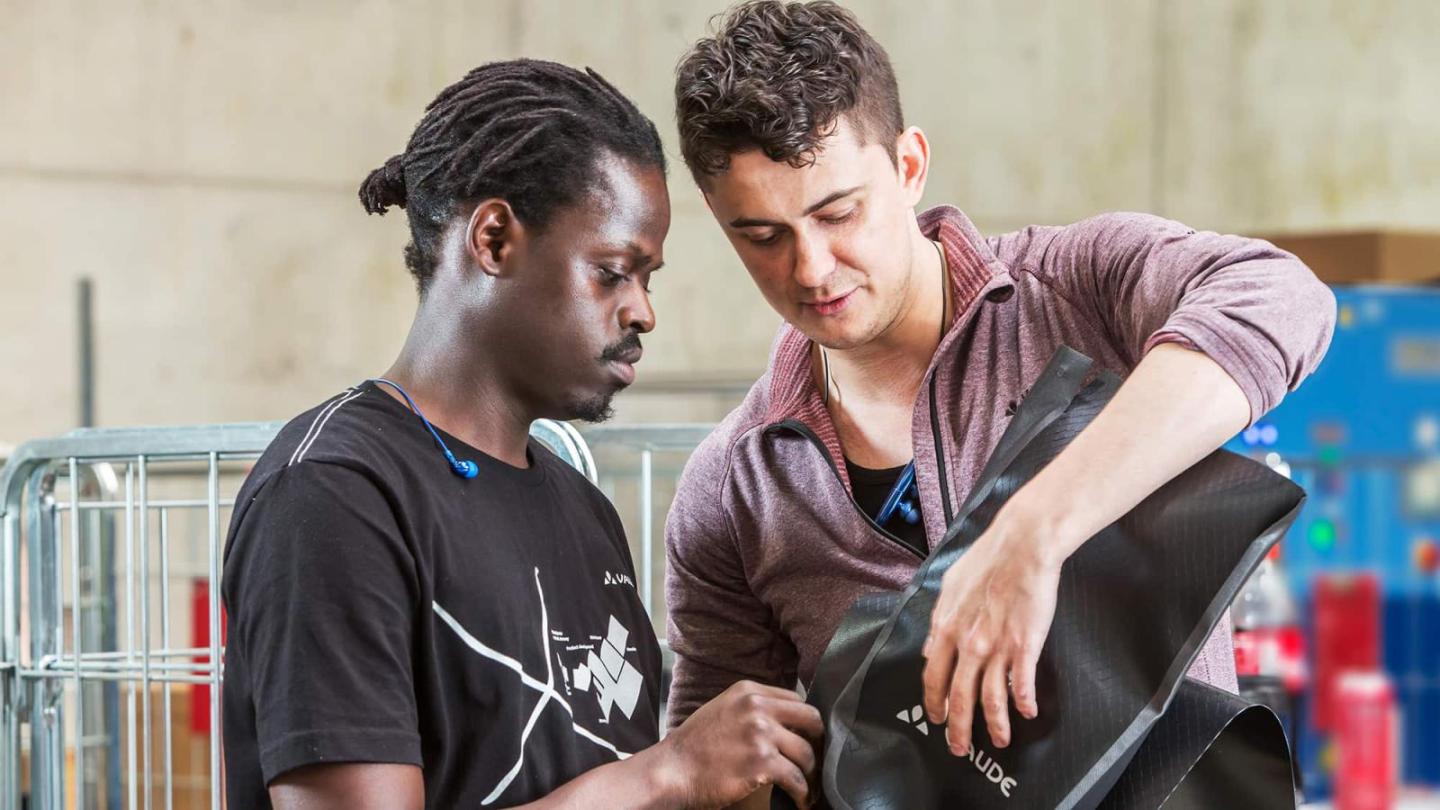 Two men in a workshop or production hall examine a piece of black material together.