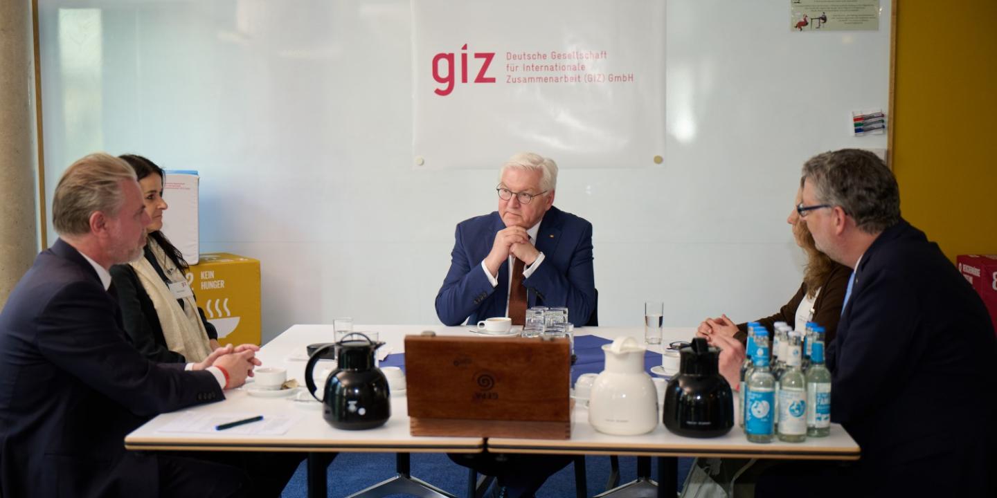 Mr. Steinmeier and Mr. Schäfer-Gümbel in conversation with GIZ employees, sitting around a table with drinks.