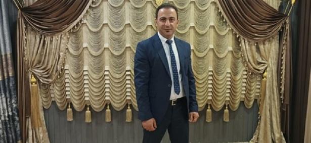 A man wearing a suit and tie is standing in front of artistically draped curtains in gold, beige and brown hues.