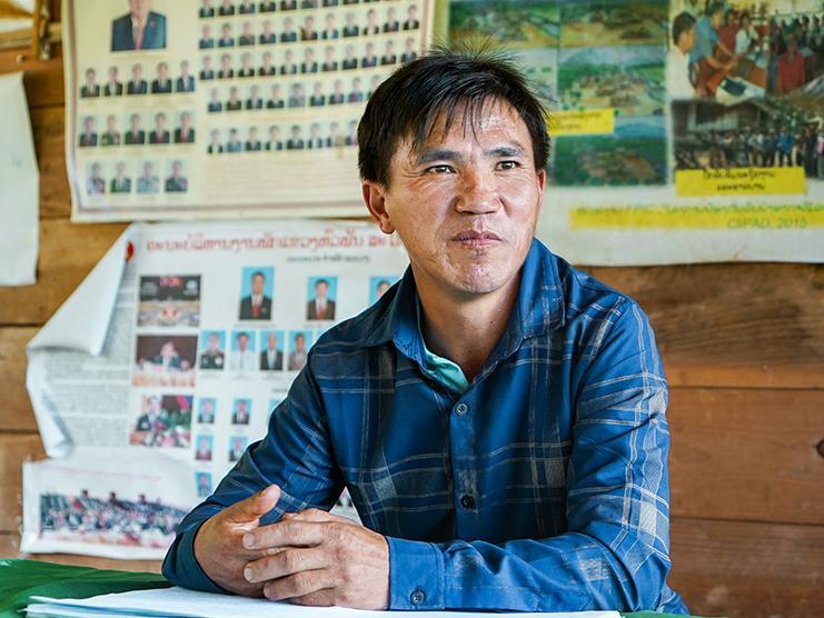 A man is sitting at a table, behind him is a wooden wall with posters.