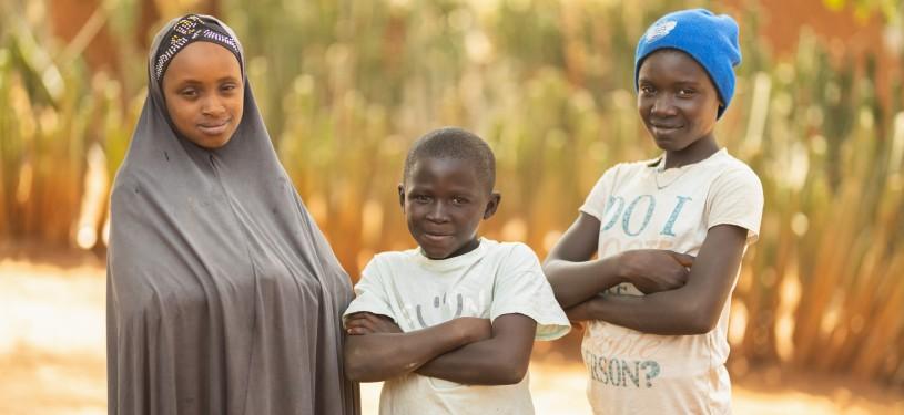 Three children are standing in front of a field.