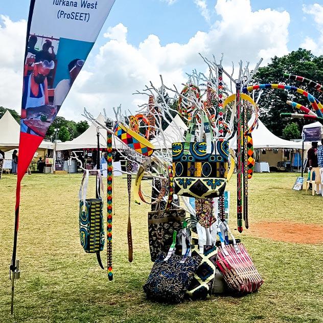 An outdoor exhibition stand with a rack full of brightly coloured bags made from recycled materials. Next to the stand is a ProSEET project banner.