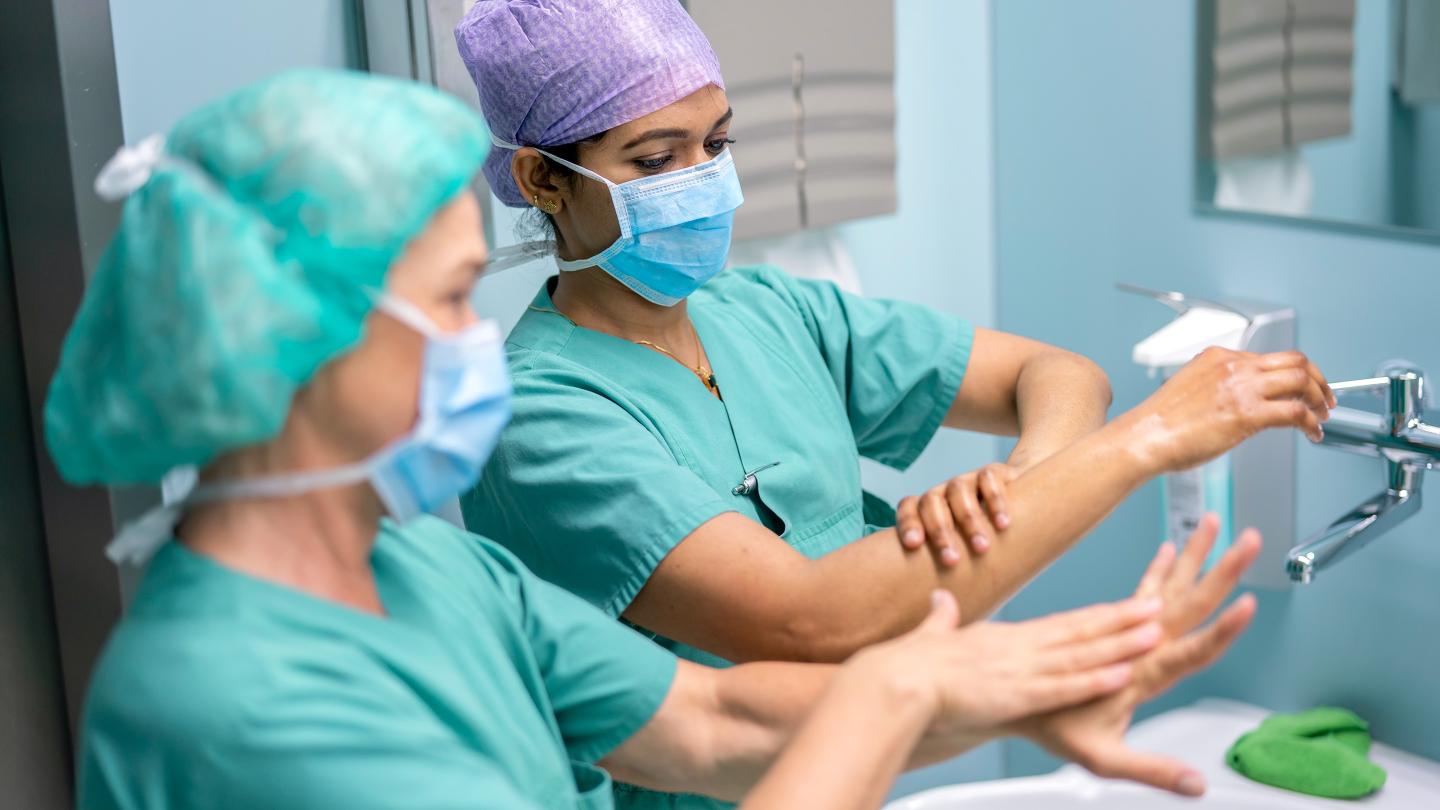 Two surgical staff members perform thorough hand disinfection in front of a mirror.