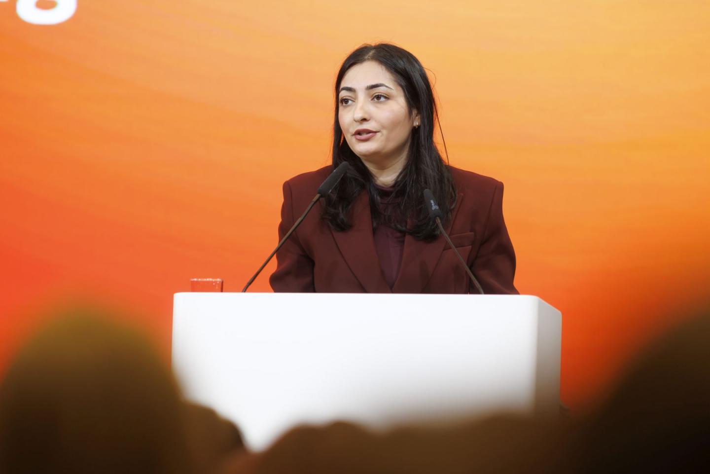 A woman stands talking at a white lectern