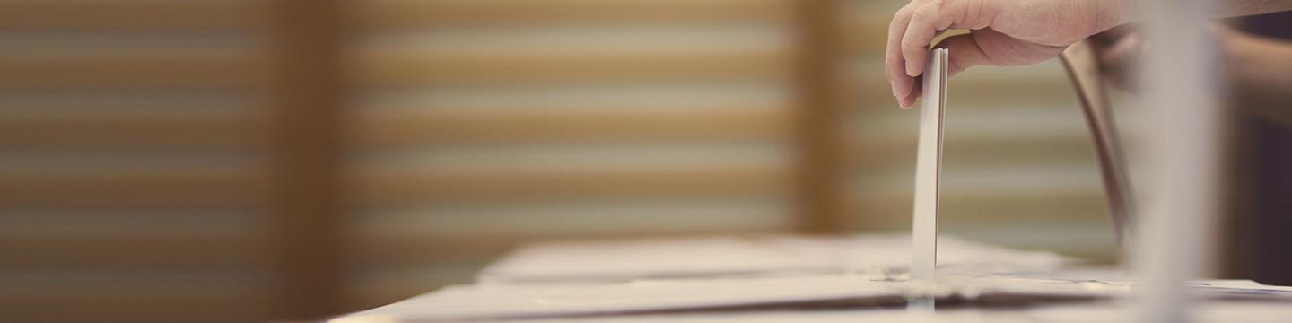 Eine Person wirft einen Stimmzettel in eine Wahlurne.