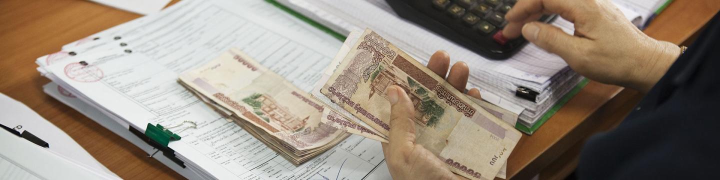 Eine Person hält Geld in der Hand und tippt auf einem Taschenrechner.