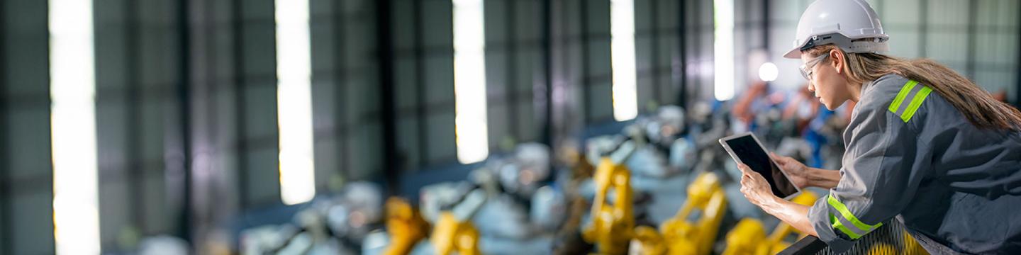 Eine junge Fabrikarbeiterin in Schutzkleidung schaut auf ein Tablet