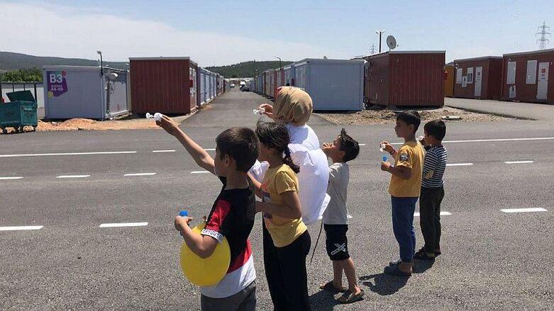 Children and a woman blow soap bubbles at a container camp.