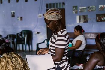 A woman stands in a room with other women and recites something.