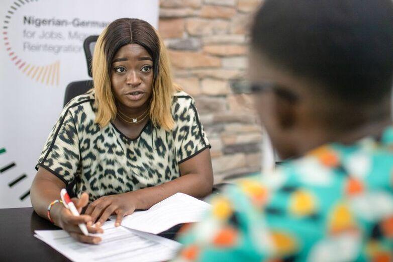 A woman sits opposite someone and fills out documents with them.