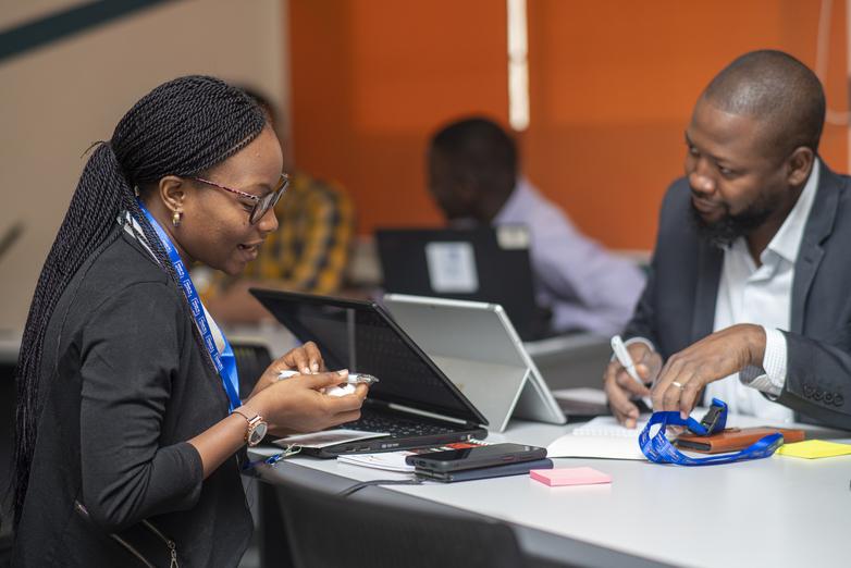 A woman and a man sitting at a modern table using digital devices.