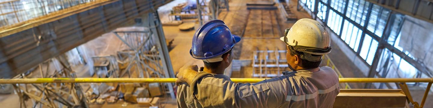 Zwei ägyptische Bauarbeiter schauen in eine Fabrikhalle hinab.