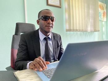 A visually impaired man sits in front of a computer in an office.