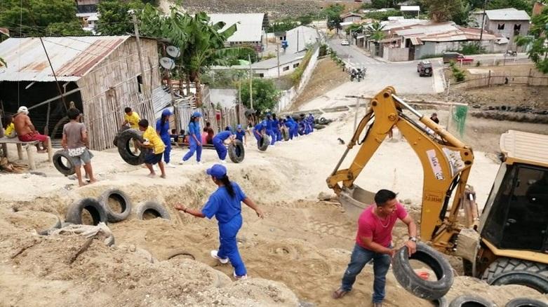 A building site with an excavator. People transport car tyres in a chain.