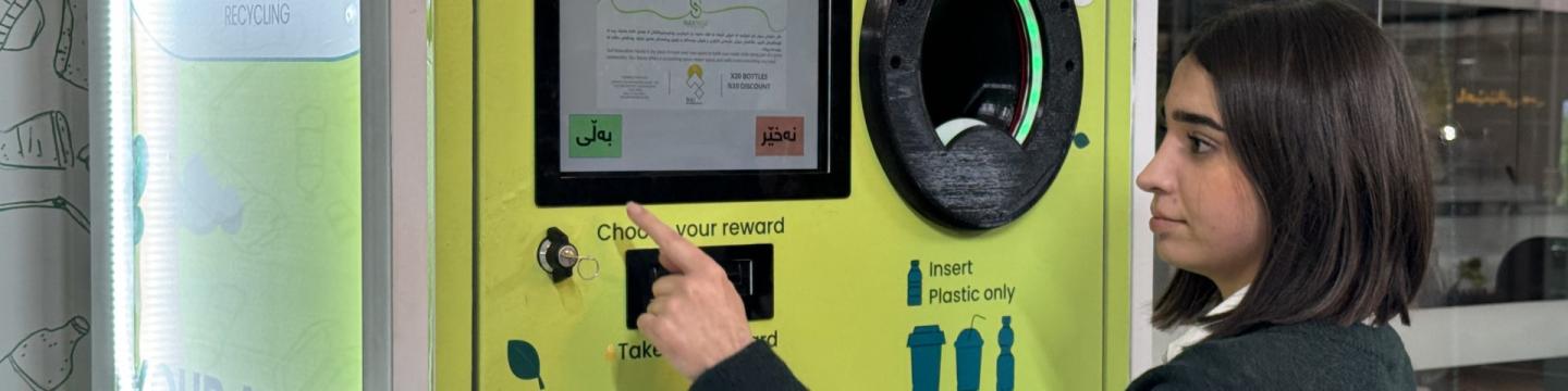 Eine junge Frau bedient einen Geldeinzahlungsautomat.