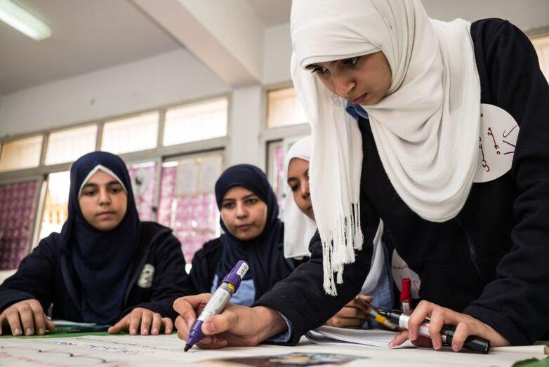 Four girls write on a poster for a group project.
