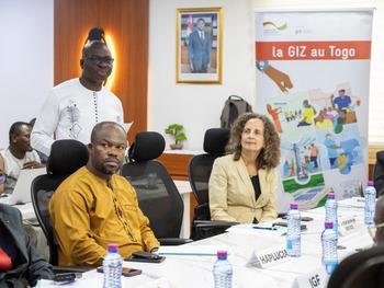 Two men and a woman in a meeting room in front of a GIZ poster.