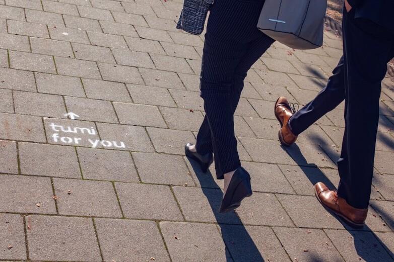 Two people walk along a pavement with ‘tumi for you’ spray-painted on it.