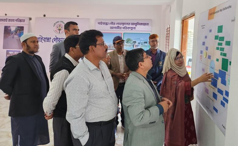 A group of people stand around a whiteboard and discuss ideas and information together.