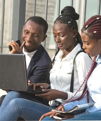 Two young women and a man sit side by side, looking at a laptop.