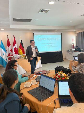 Ein Mann referiert bei einer Veranstaltung vor Menschen mit Laptops und Notizzetteln.