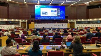 People sitting in a large hall, watching a presentation on a screen.