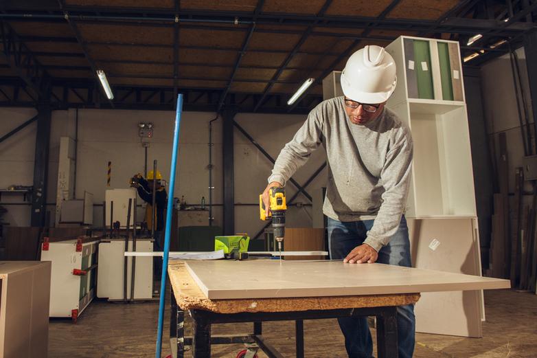 A female worker in a greenhouse inspecting the underside of a sheet on which lettuce is growing.