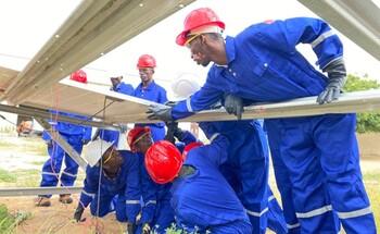 Auszubildende in blauen Uniformen und roten Helmen bei der Installation von Solarmodulen während einer Schulung zu erneuerbaren Energien in Somalia.