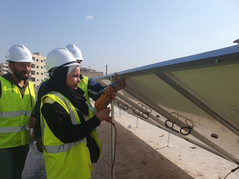 A group of people work together to install a solar panel outdoors.