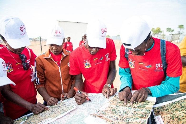 Four people in GIZ baseball caps marking a spot on maps of an informal settlement. Copyright: GIZ