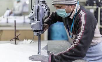 A textile worker wears a protective mask and works on a piece of furniture.