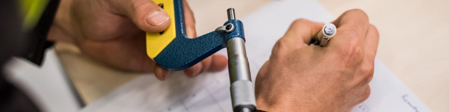 Eine Person hält ein technisches Messgerät in der Hand und notiert etwas auf einem Papier.