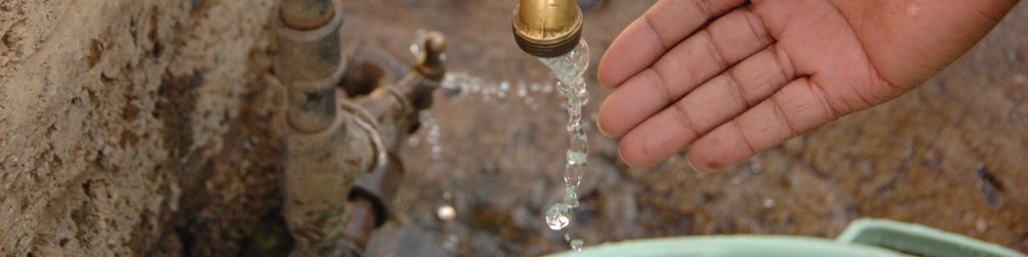 Eine Hand unter einem Hahn, aus dem Wasser fließt.