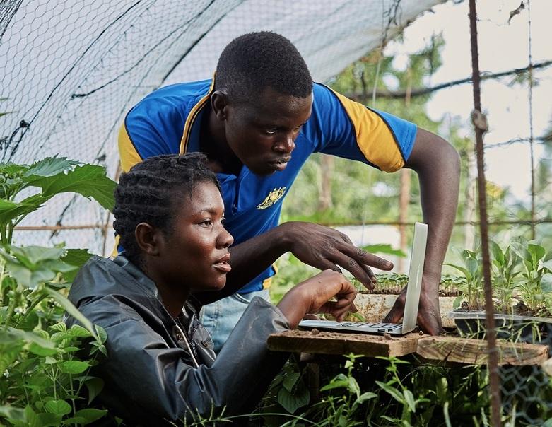 Two people look at a laptop in a greenhouse.