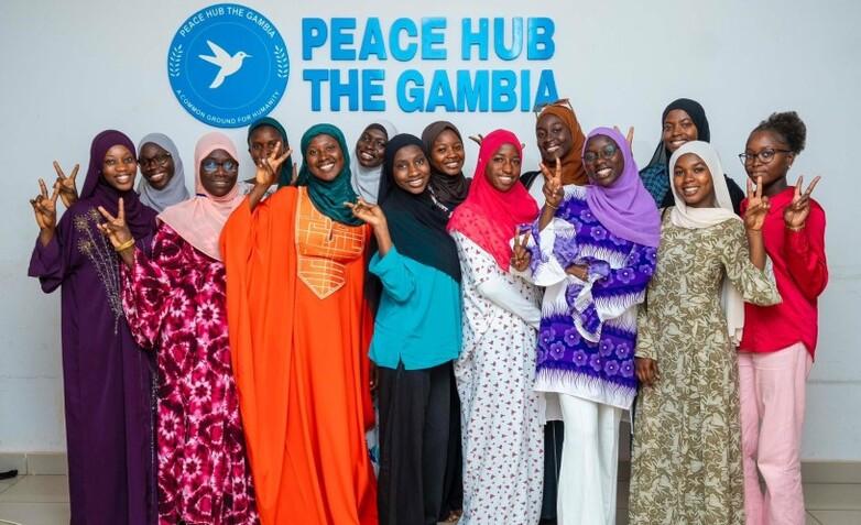 Eine Gruppe junger Frauen vor einem Schild mit der Aufschrift „Peace HUB the Gambia“.