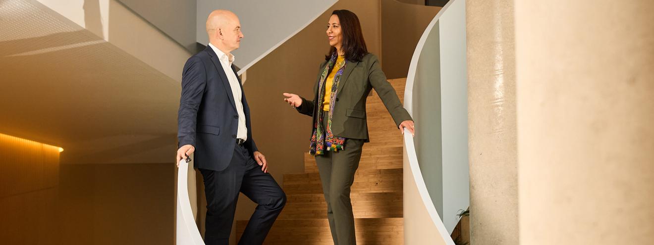 Zwei Geschäftspersonen unterhalten sich auf einer hölzernen Wendeltreppe in einem modernen Bürogebäude