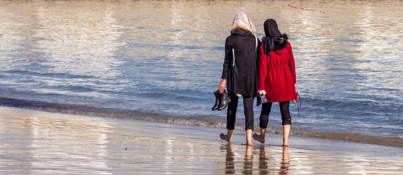 Two women walking on the beach with their backs to the viewer