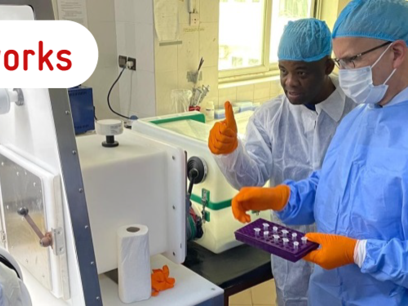 Five people in medical protective clothing and masks stand around a laboratory device.