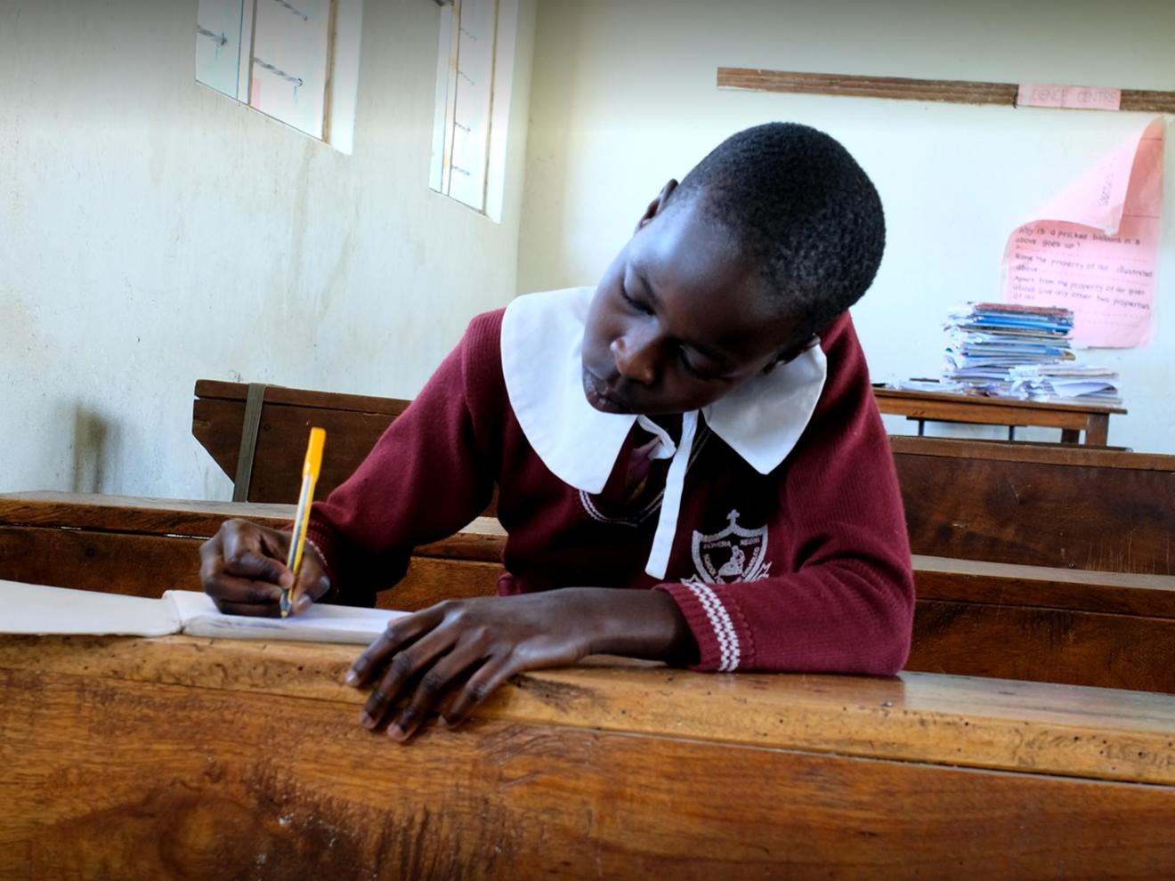 Girl sitting at a school desk writing in a notebook
