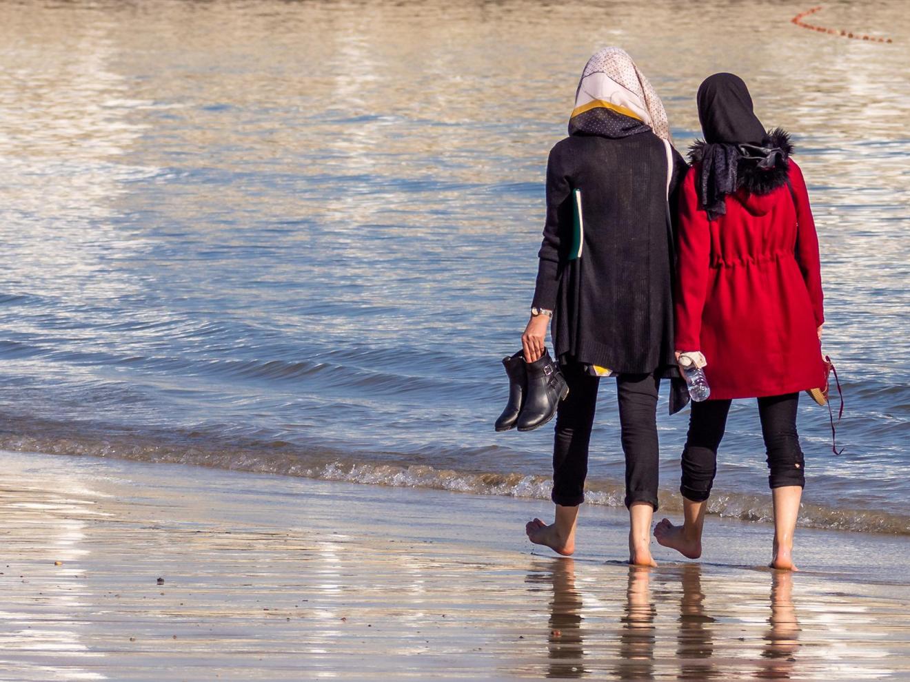 Two women walking on the beach with their backs to the viewer