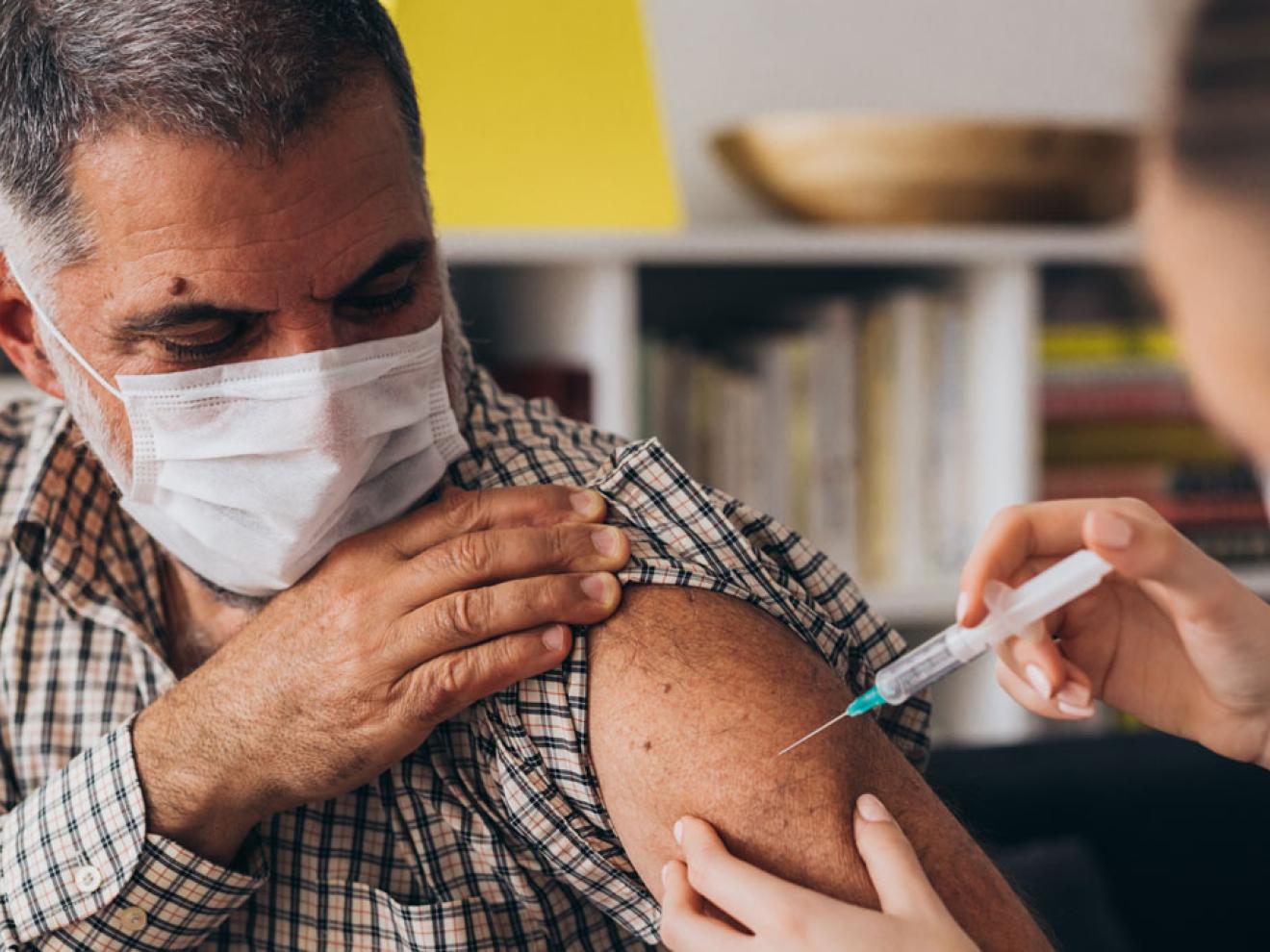 A man receiving an injection in his upper arm from a second person.