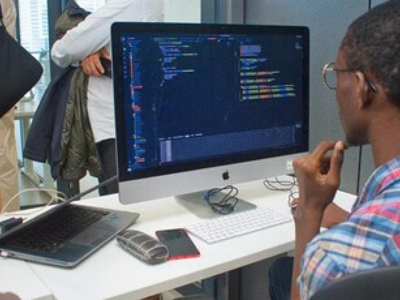 A young man programming on a computer in a classroom.